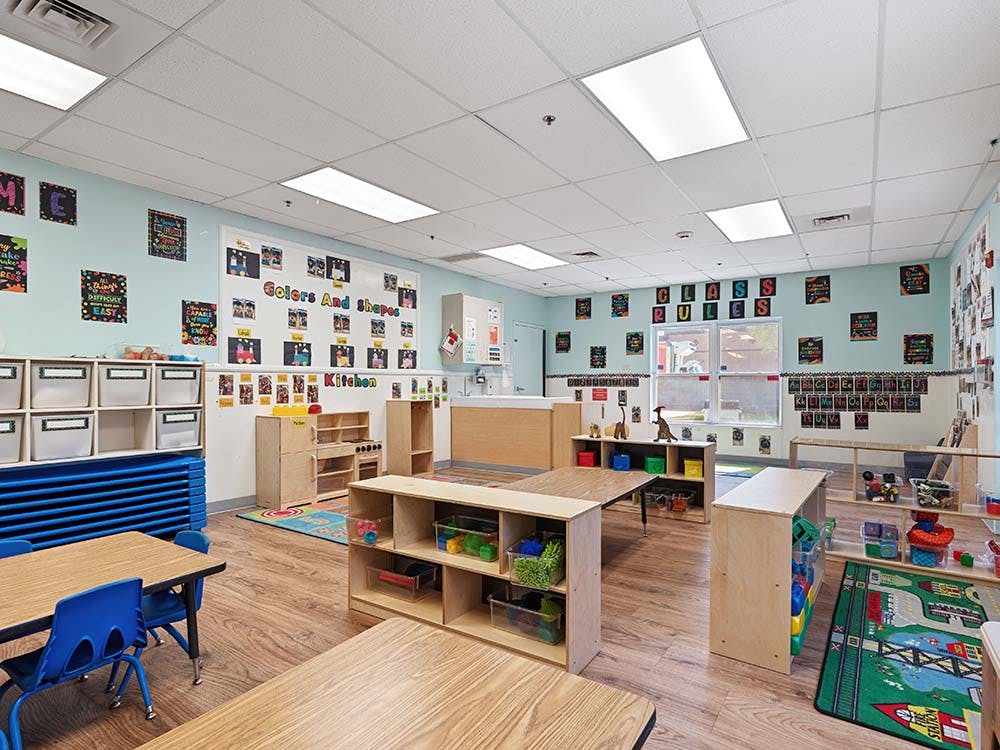 Empty classroom with small tables and chairs, shelves, and posters on the wall
