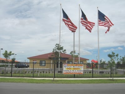 Three American flags flying on poles in front of a building with a fence