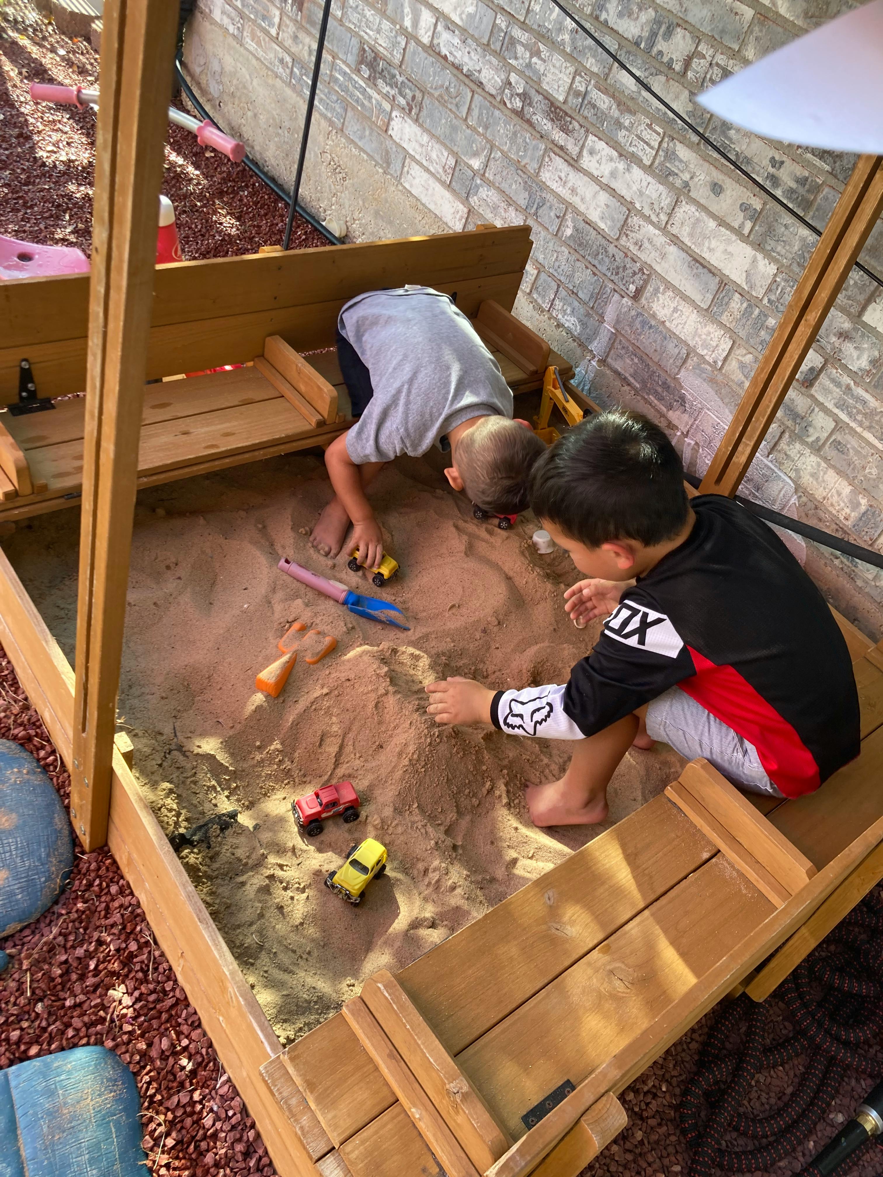 Two children playing in a sandbox with toys