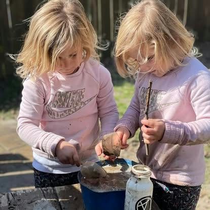 Two children playing with mud in a bucket outdoors