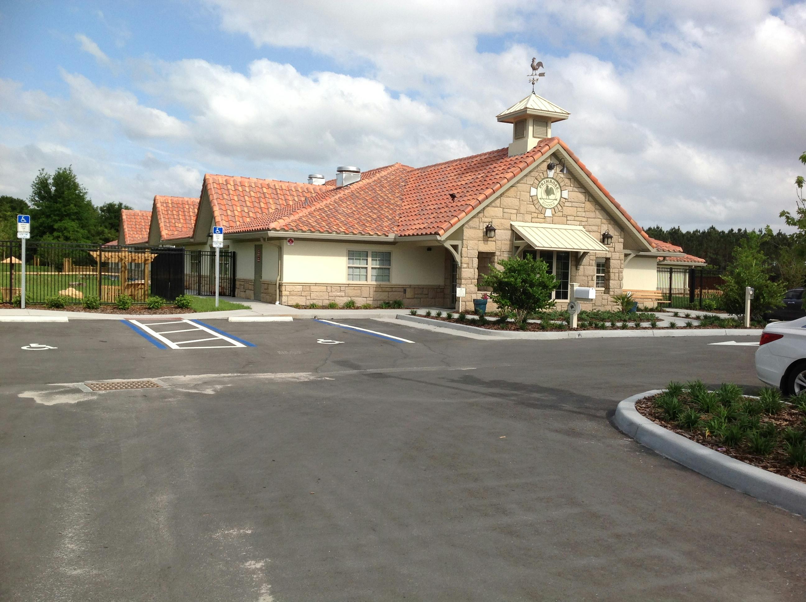 Building with a red tile roof and a small cupola, with a parking lot in front