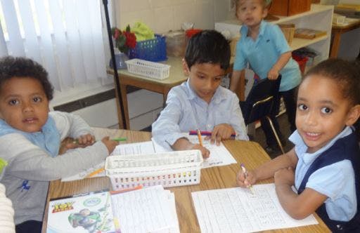 Three children writing at desks in a classroom