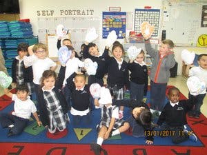 Children posing with paper cutouts on their hands in a classroom