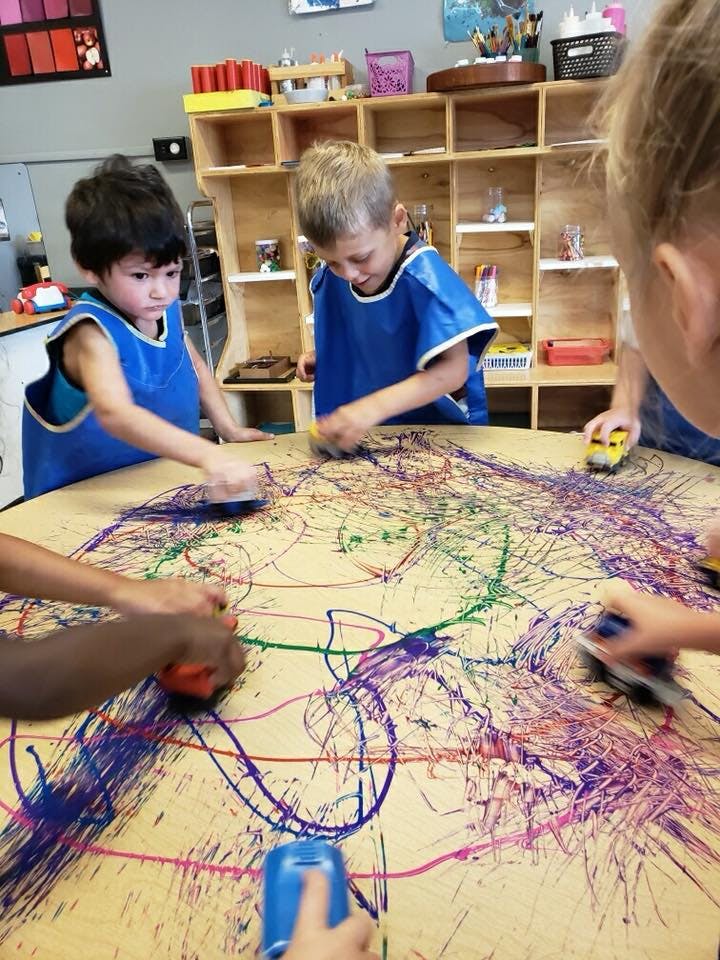 Children in blue smocks painting on a large table
