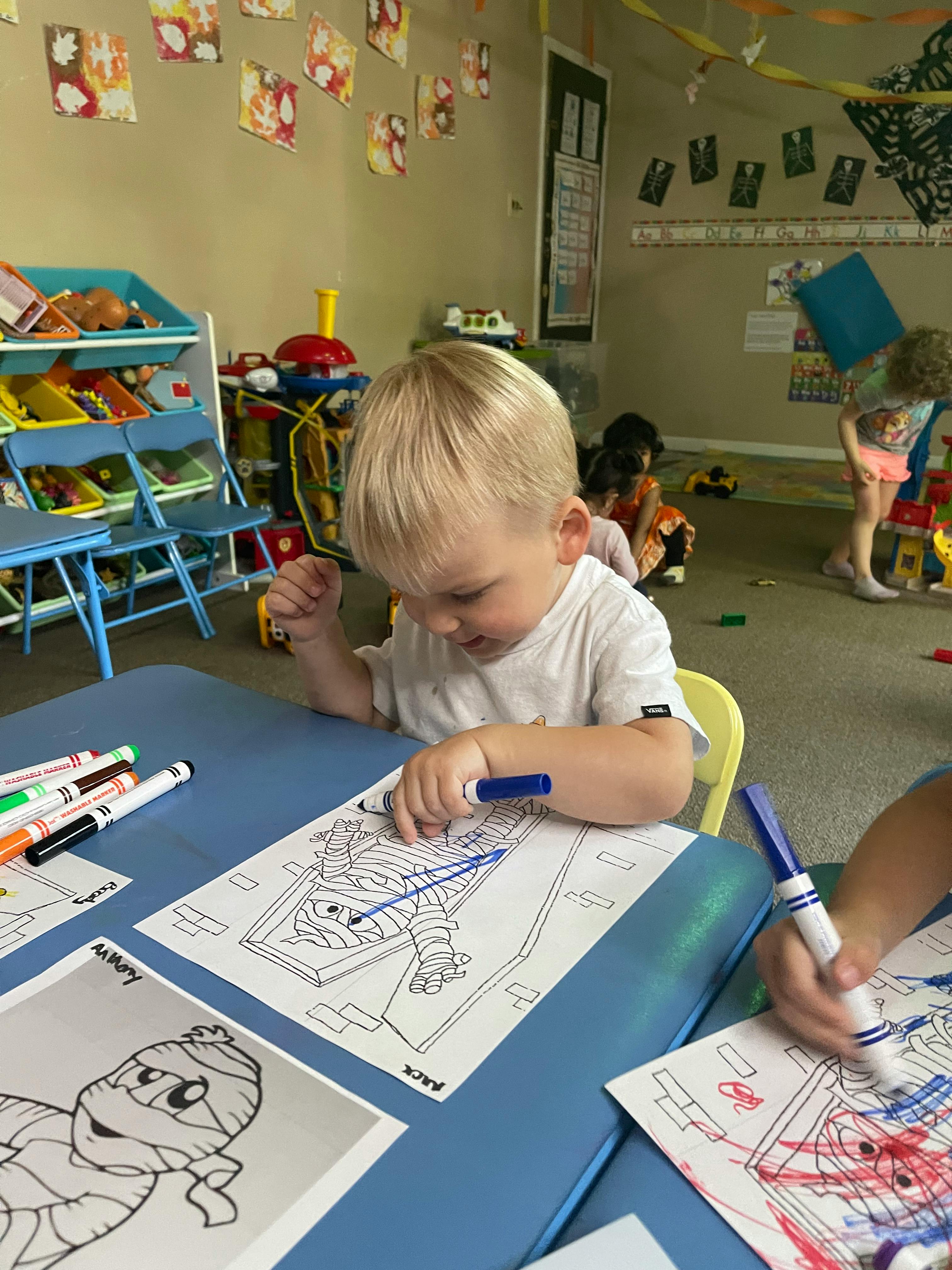Child coloring a drawing at a table in a classroom