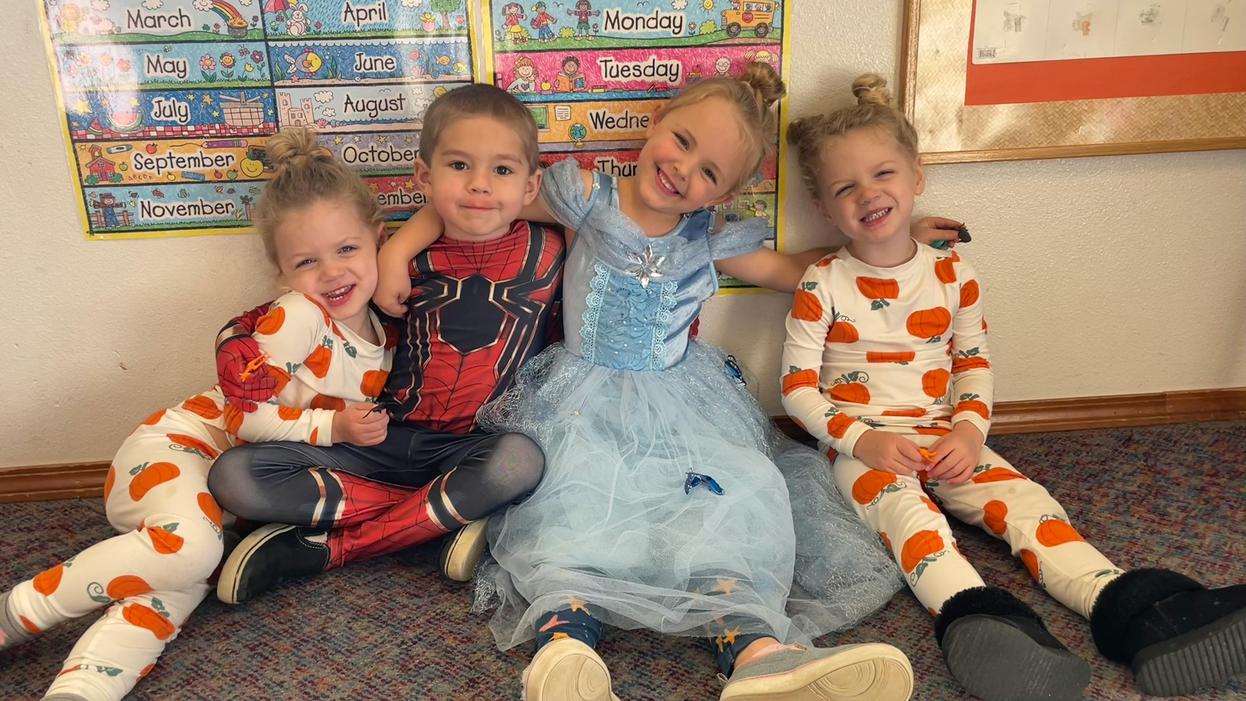 Four children sitting on the floor, two in pumpkin pajamas, one in a spider costume