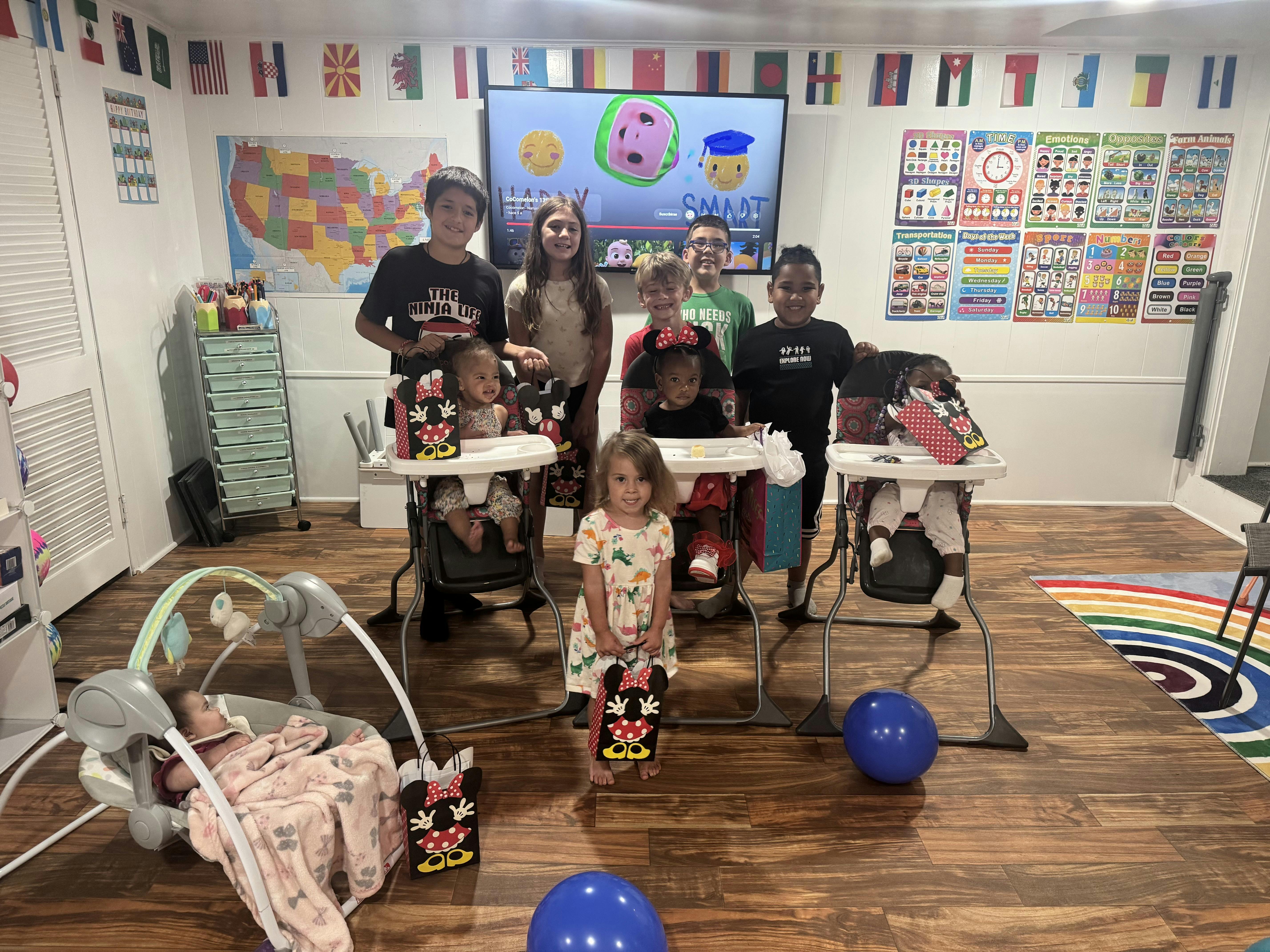 Group of children standing and sitting around a TV screen in a playroom