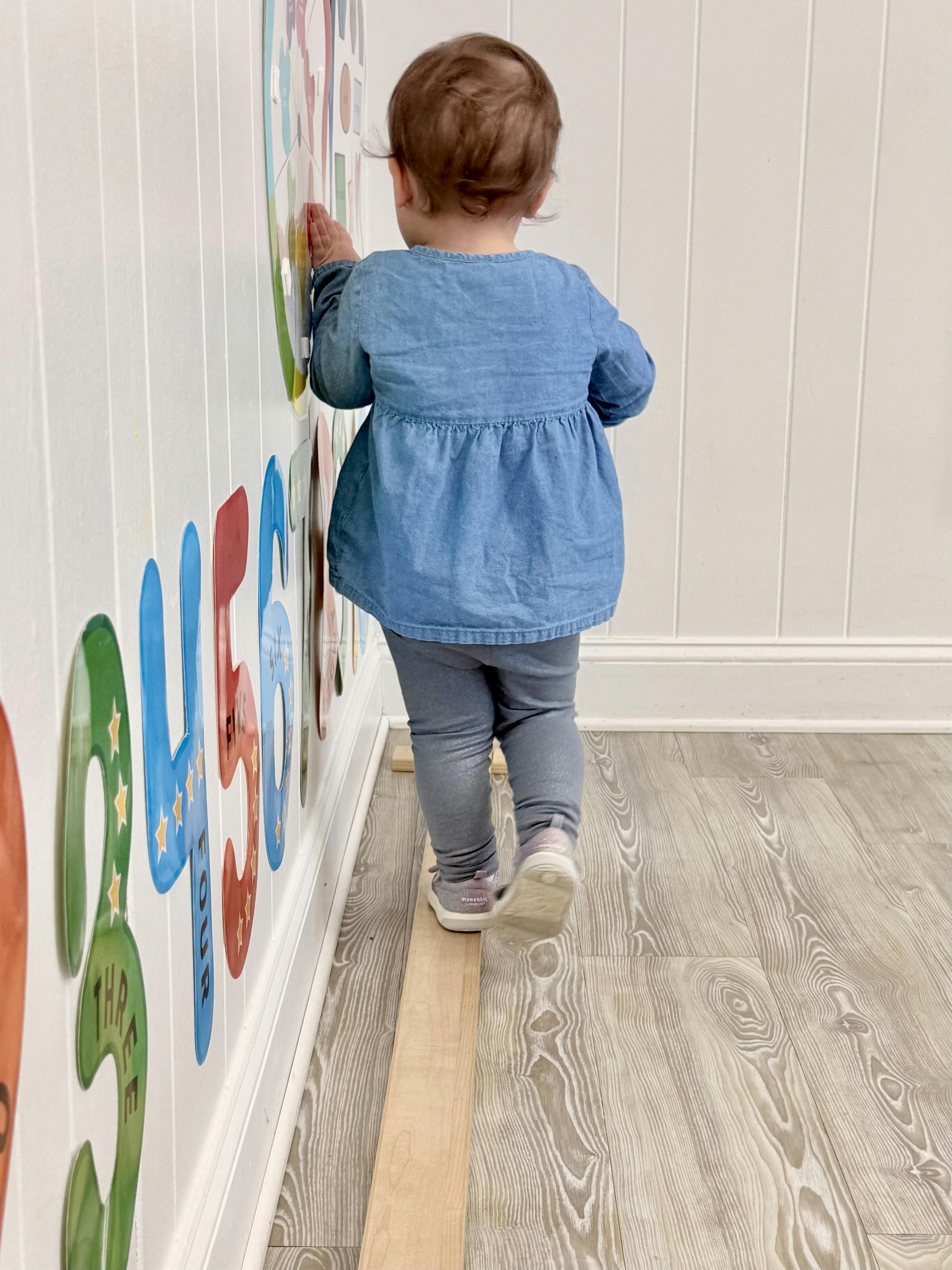 Child walking on a wooden plank next to a wall with large numbers
