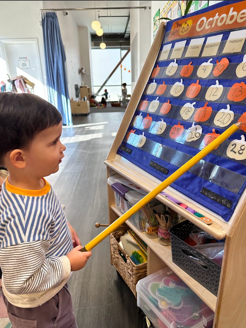 Child pointing at a calendar with a stick in a classroom