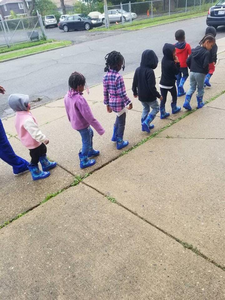 Children in blue boots walking in a line on a sidewalk