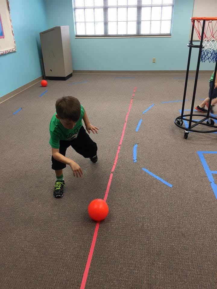 Child playing with a red ball on a carpeted floor with tape lines