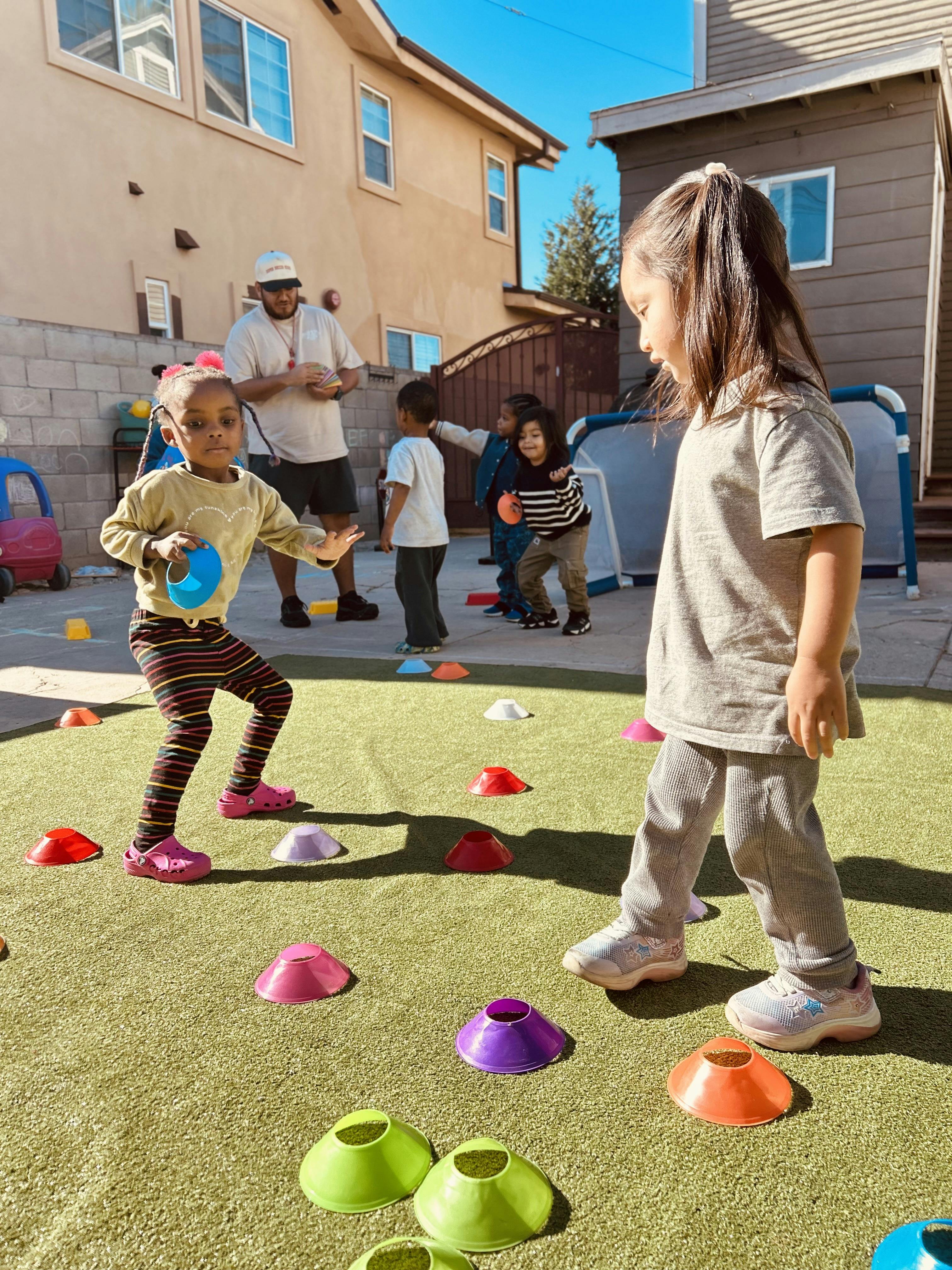 Children playing with colorful cones on artificial grass, adult supervising