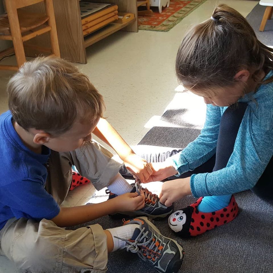 Two children sitting on the floor tying shoelaces