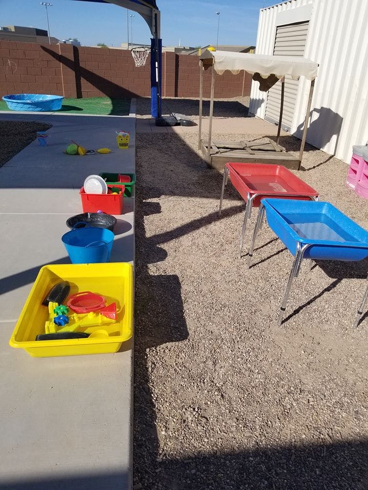 Outdoor play area with water tables, sand toys, and a basketball hoop