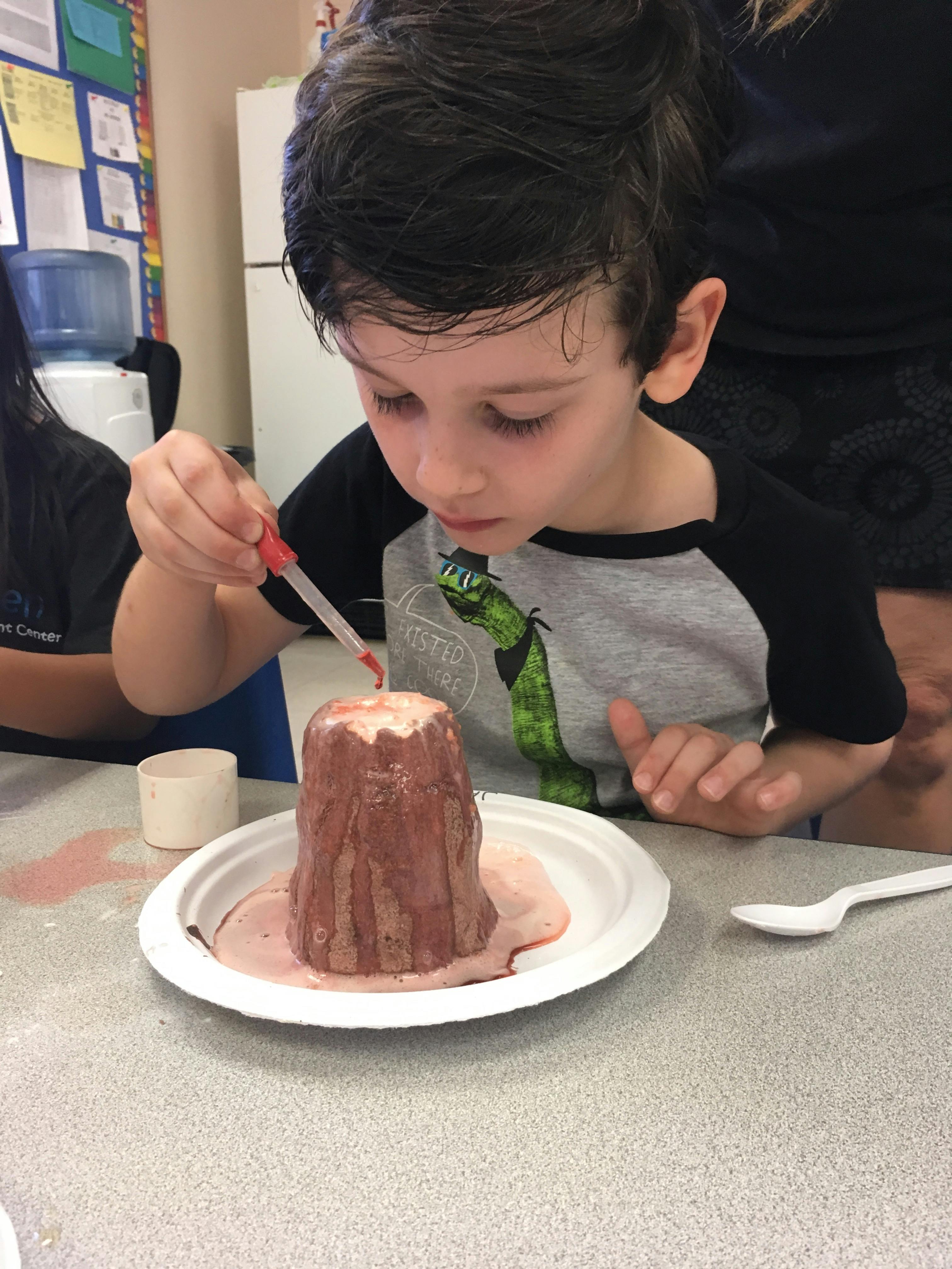 Child using a dropper to add liquid to a small volcano model
