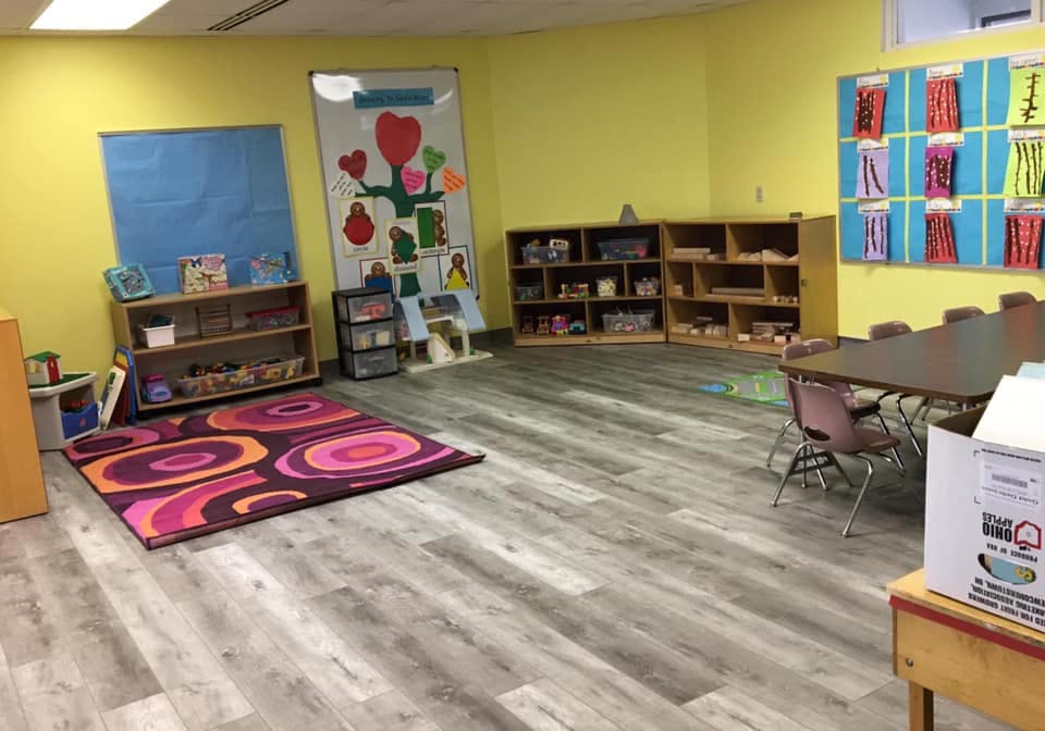 Empty classroom with tables, chairs, shelves, and a colorful rug