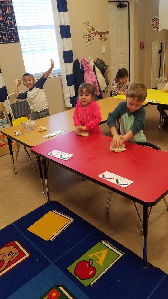 Children playing with dough at tables in a classroom