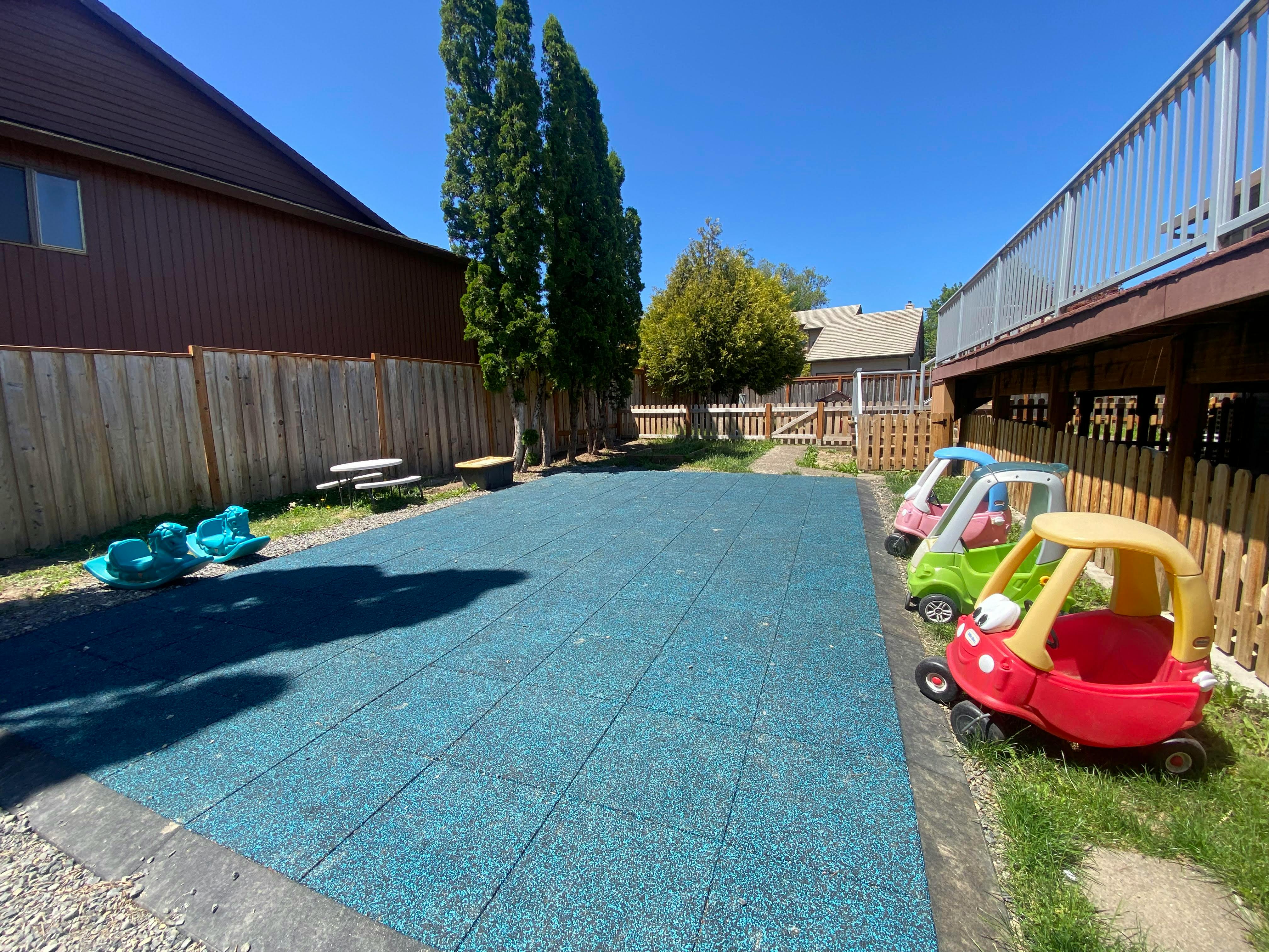 Outdoor play area with blue mat, toy cars, and rocking toys