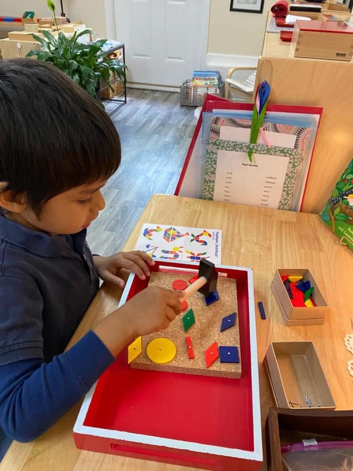 Child playing with a hammer and geometric shapes on a corkboard