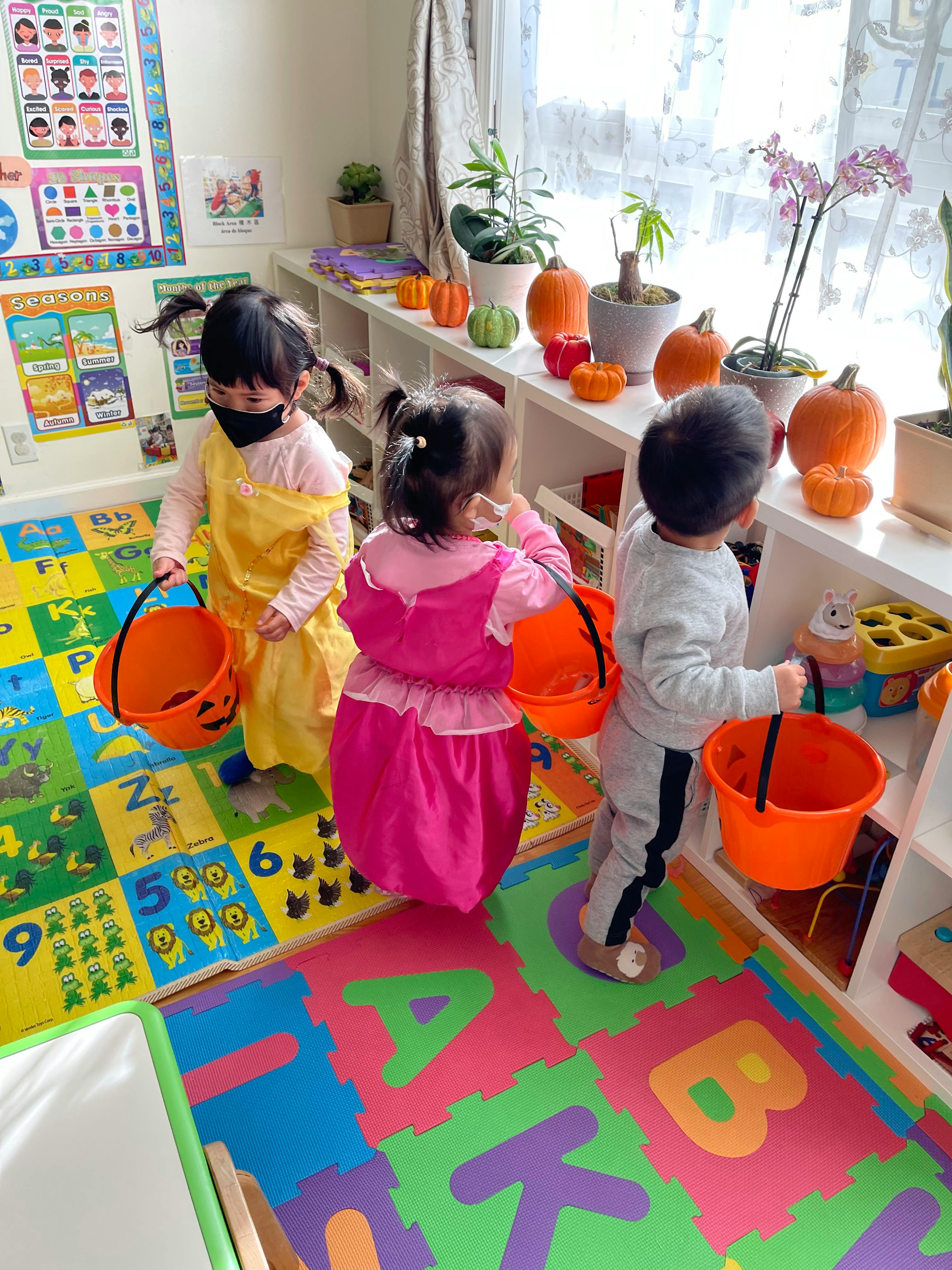 Three children with orange buckets in a classroom with pumpkin decorations