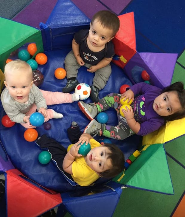 Four children playing with balls in a soft play area