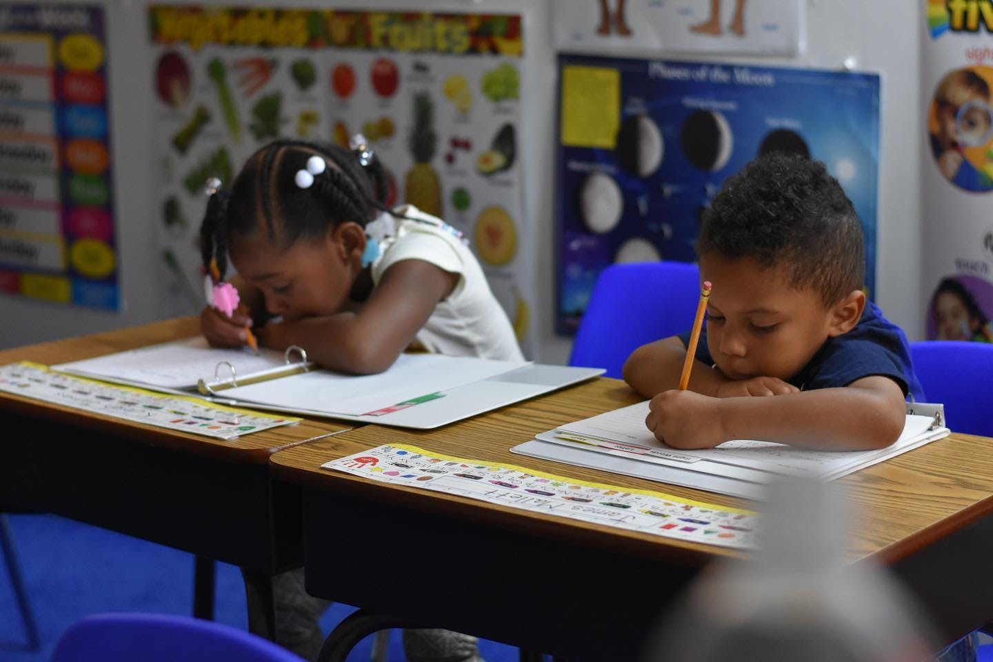 Two children writing at desks in a classroom