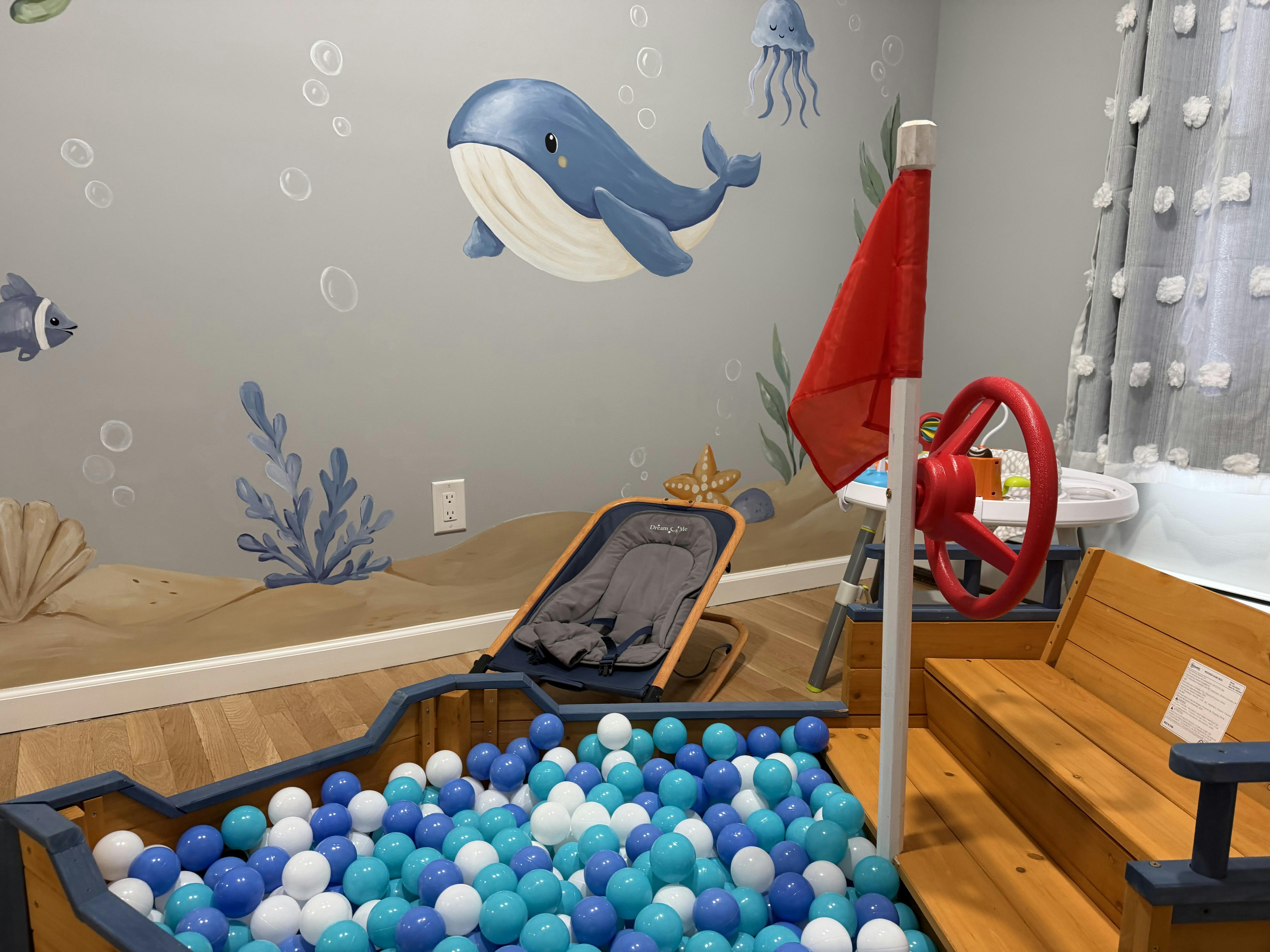 Wooden boat ball pit with blue and white balls in a room with ocean wall art