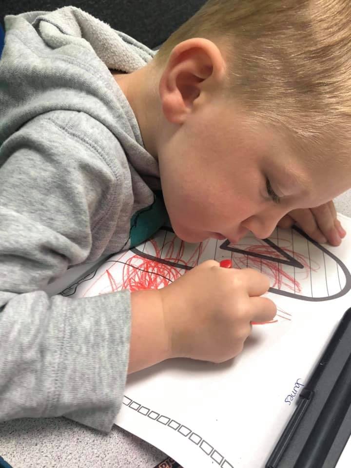 Child coloring on paper with a red crayon