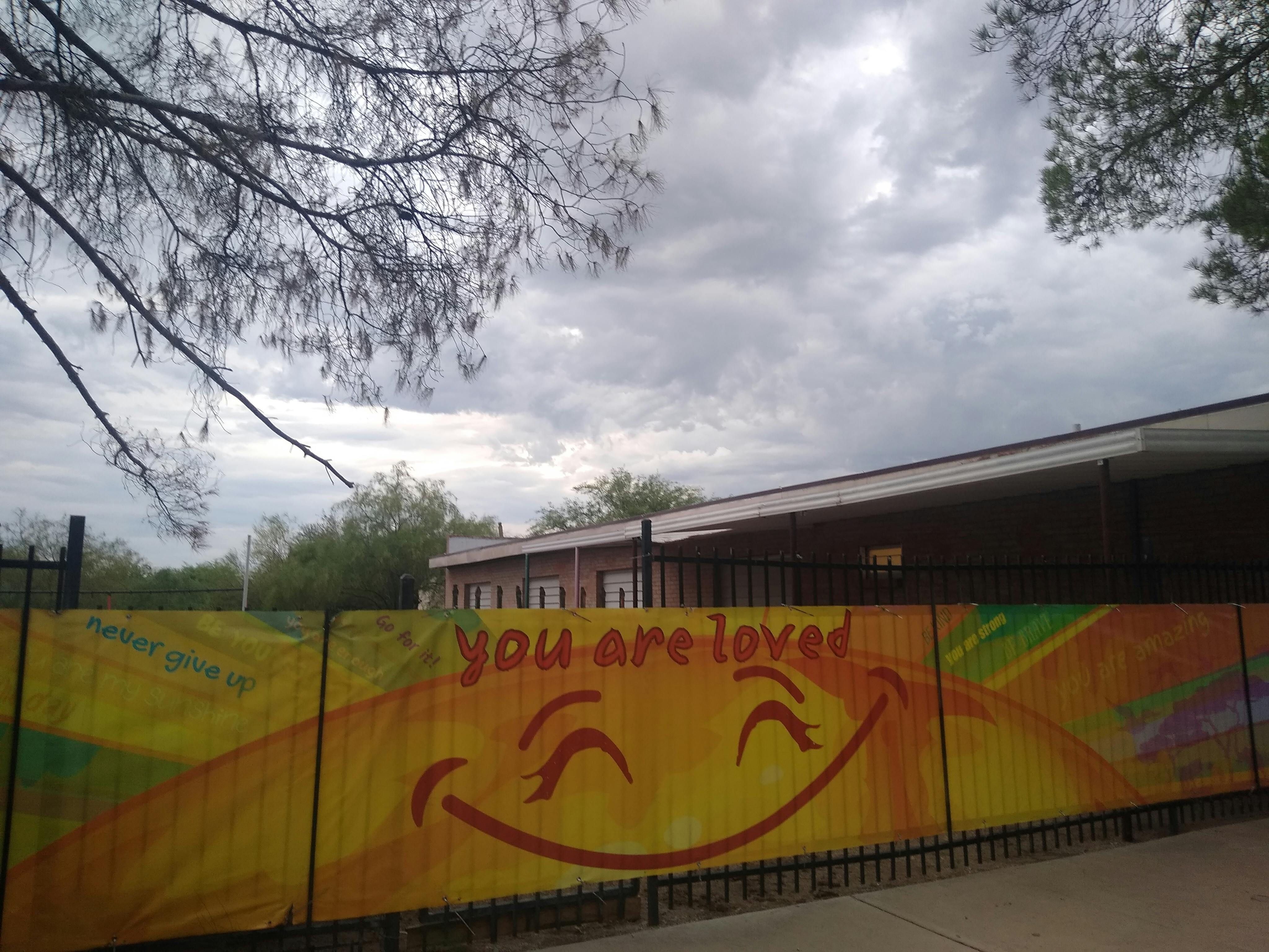 Yellow fence banner with a smiling sun and the words you are loved