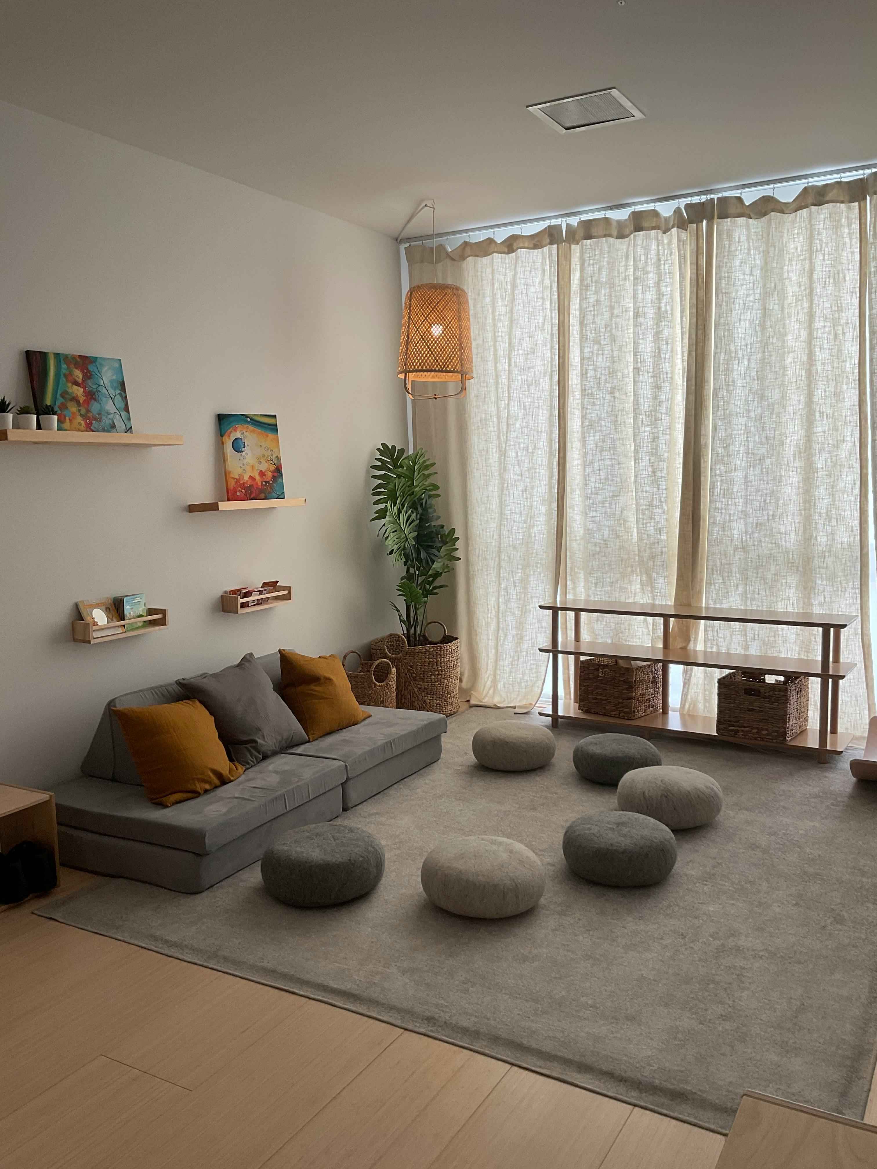 Living room with a gray sectional sofa, floor cushions, and sheer curtains