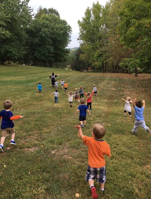 Children running on a grassy hill with trees in the background