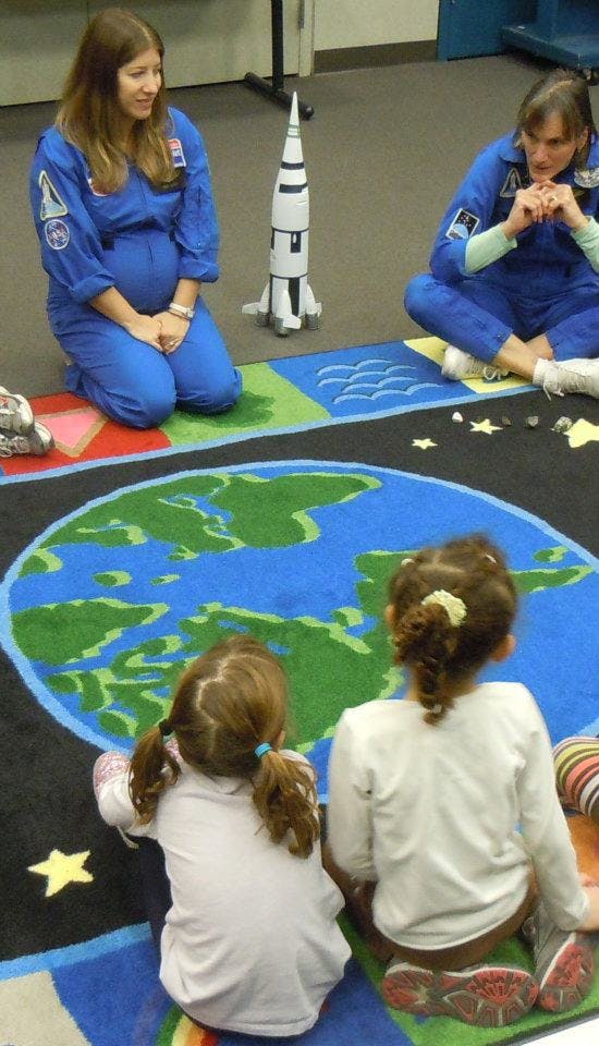 Two people in blue jumpsuits with two children on a rug with a world map