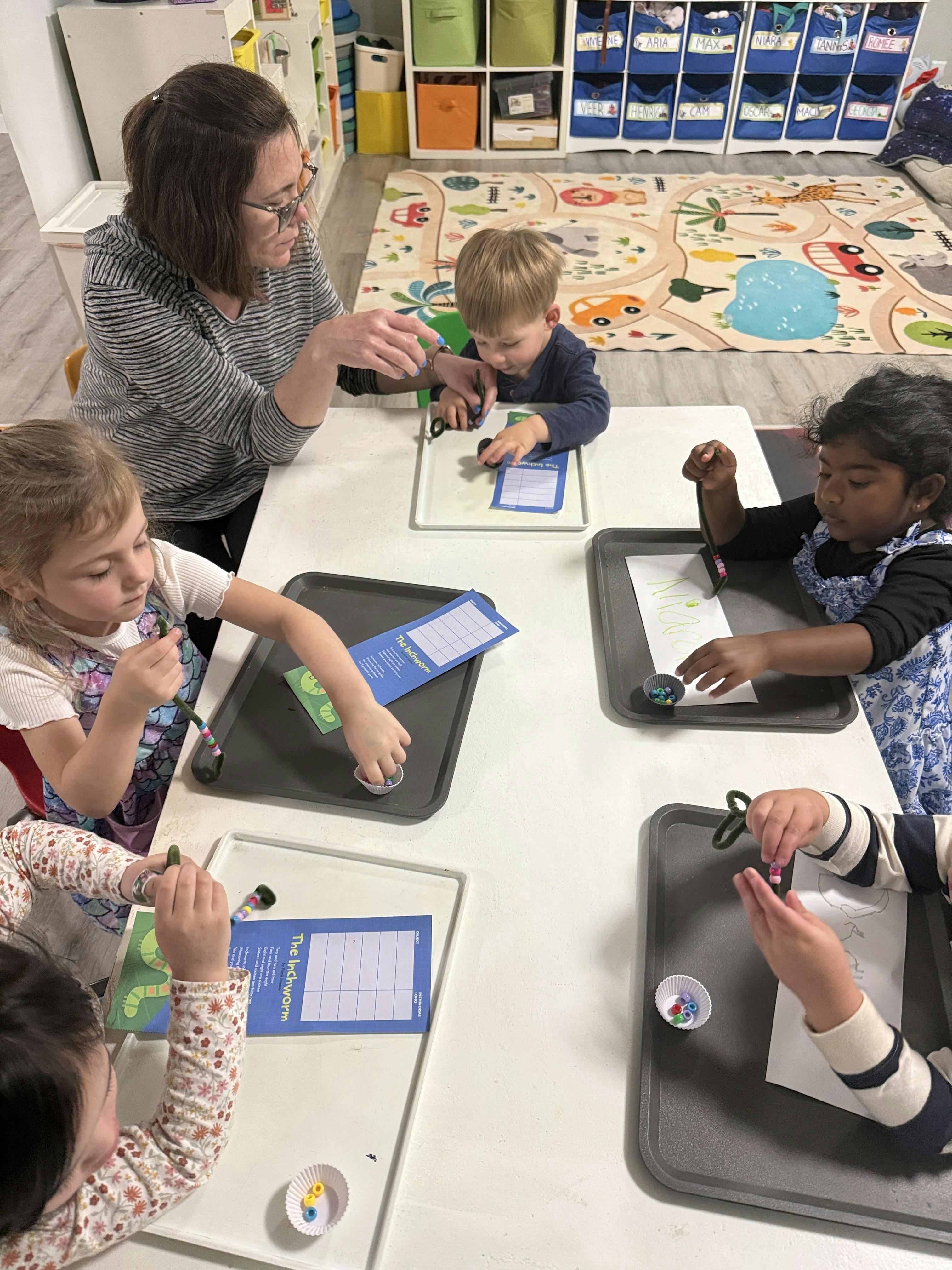Teacher and children threading beads onto pipe cleaners at a table