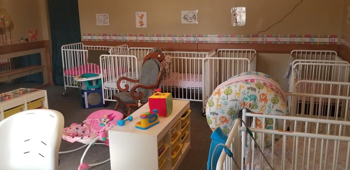 Room with multiple white cribs and baby items