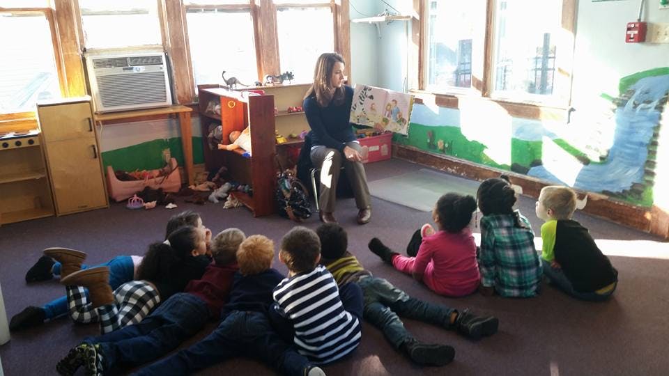 Person reading a book to a group of children in a classroom