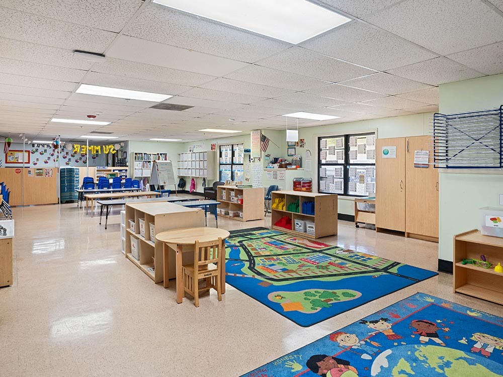 Empty classroom with small tables and chairs, colorful rugs on the floor rugs, and storage cabinets