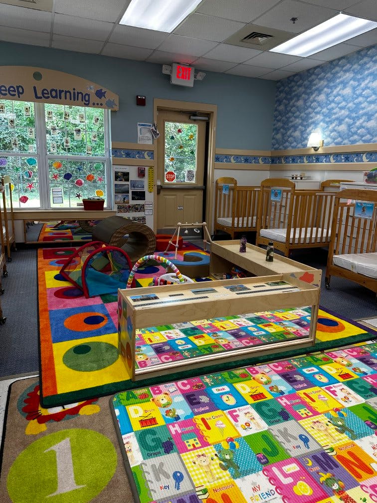 Colorful playroom with cribs, play mats, and a window with a valance that says "Keep Learning"