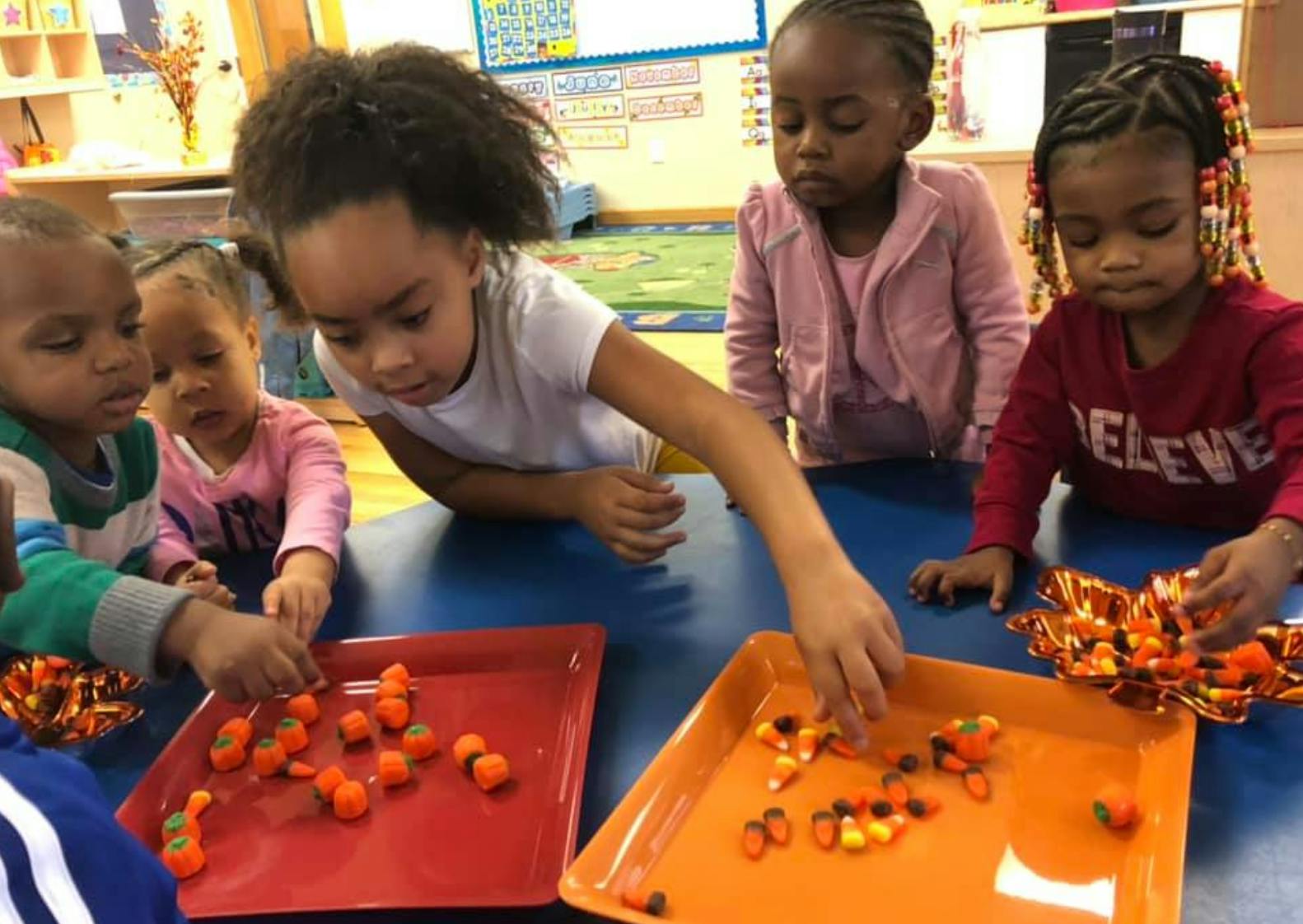 Children playing with candy corn and pumpkin candies on trays