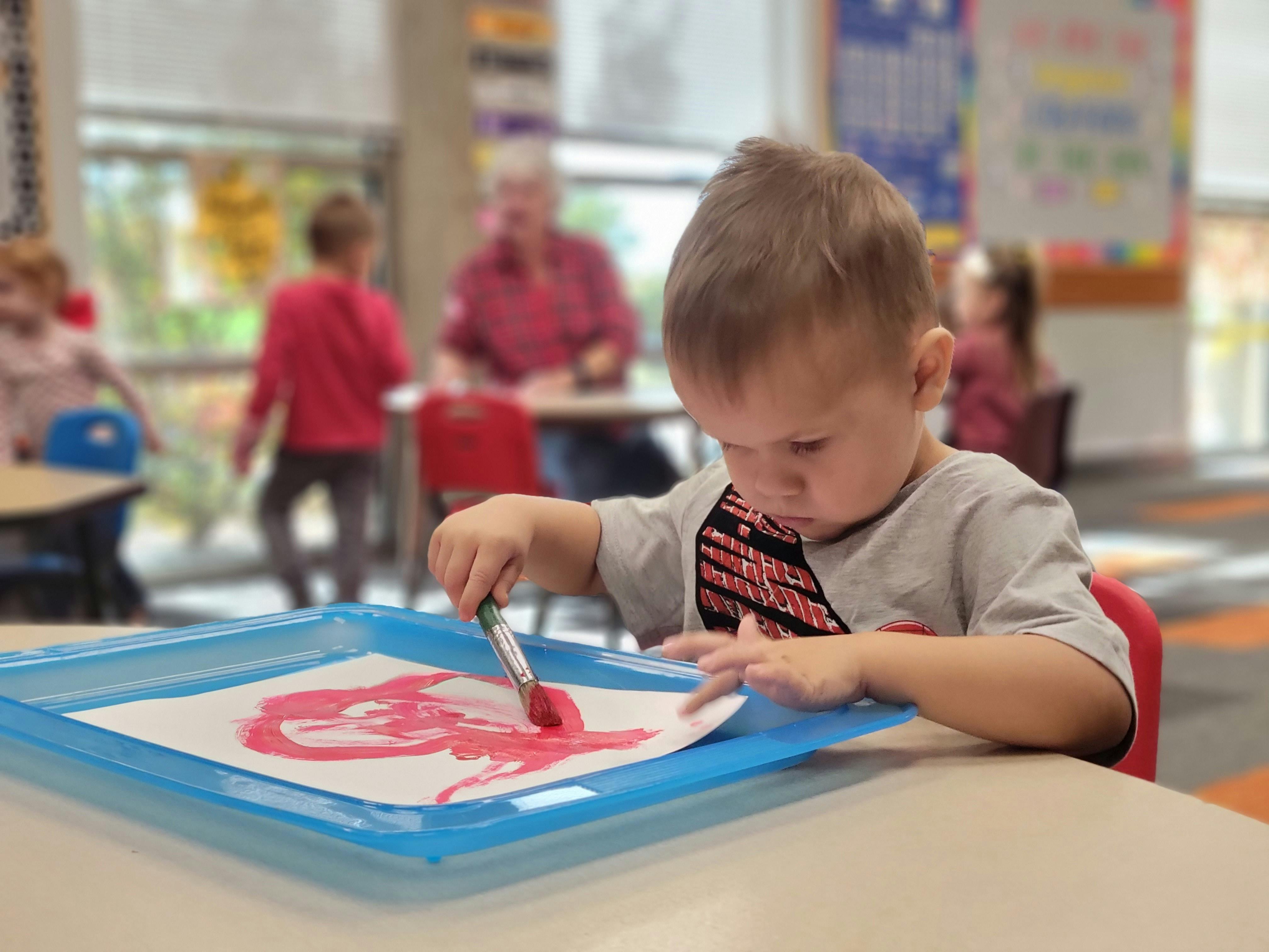 Child painting with a brush on paper in a classroom