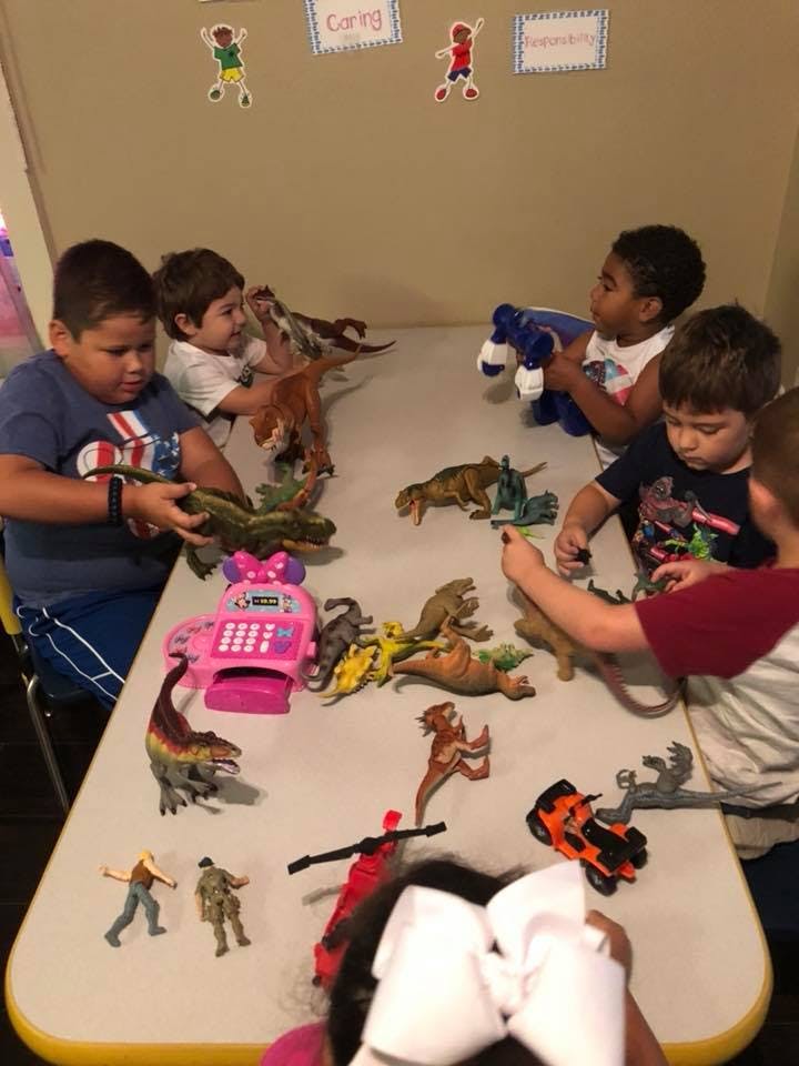 Children playing with dinosaur toys and other figures on a table