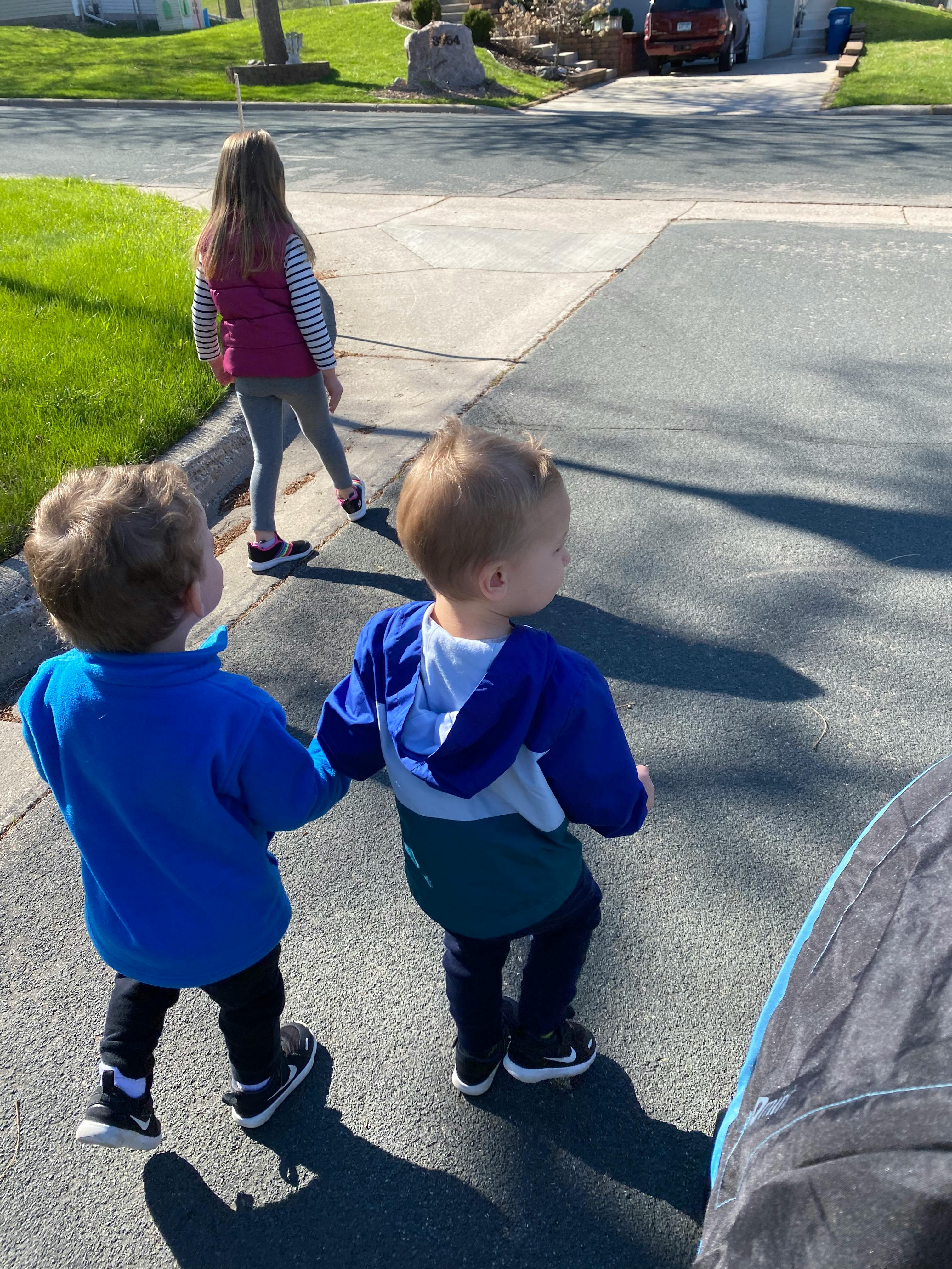 Two children walking on a sidewalk with a teen walking ahead
