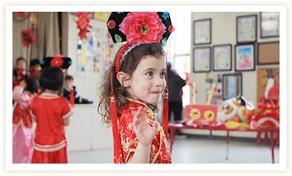 Child in traditional clothing with a floral headpiece waving