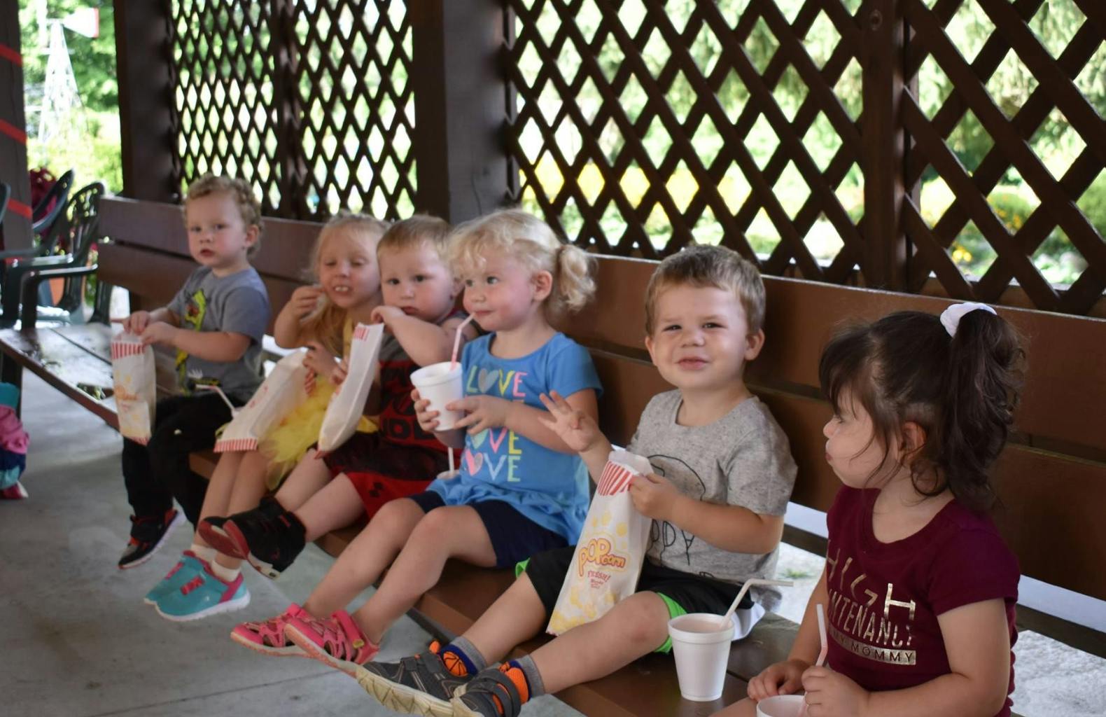 Group of children sitting on a bench holding snacks and drinks