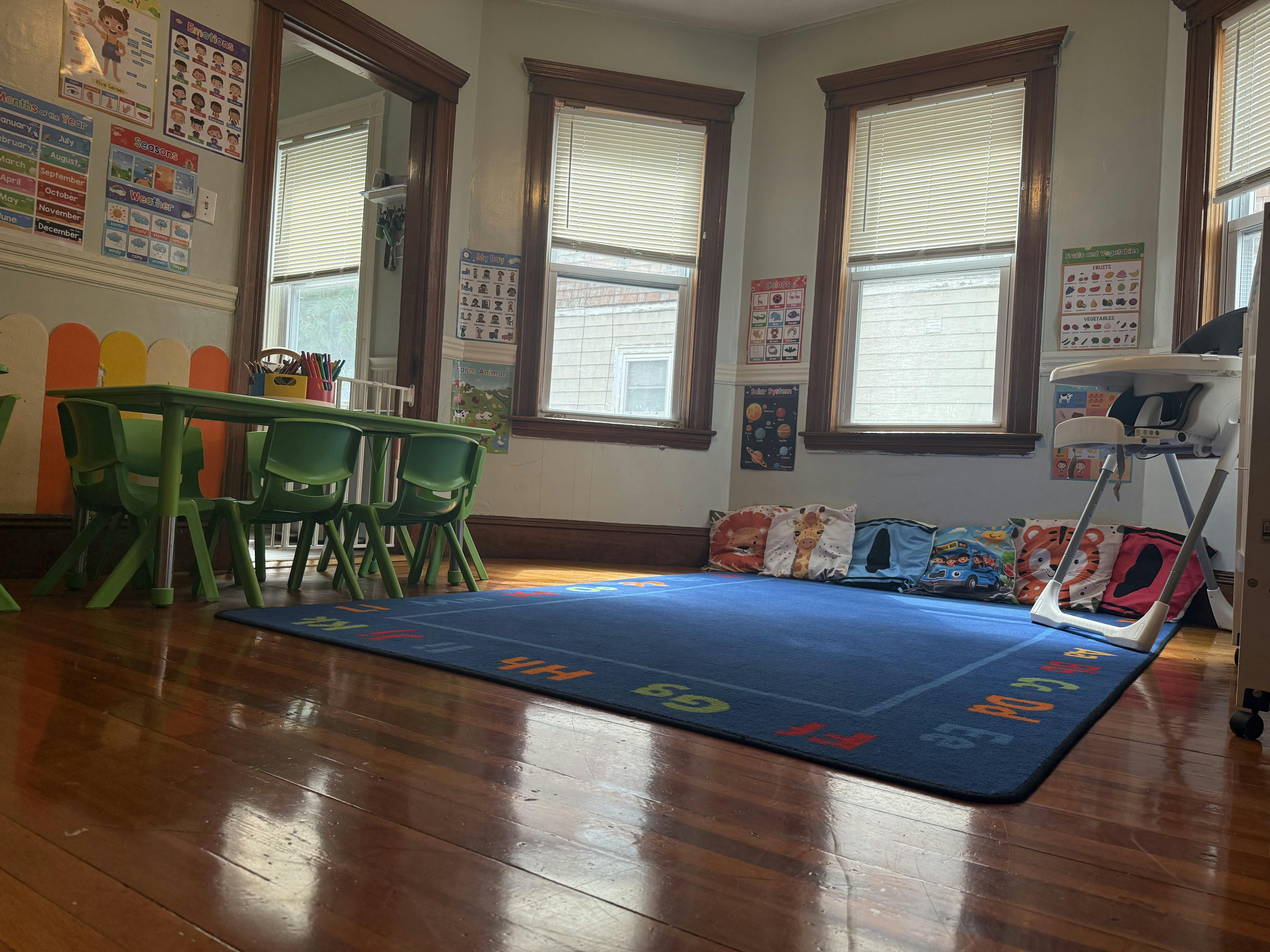Childcare room with a small table, chairs, play area rug, and wall posters