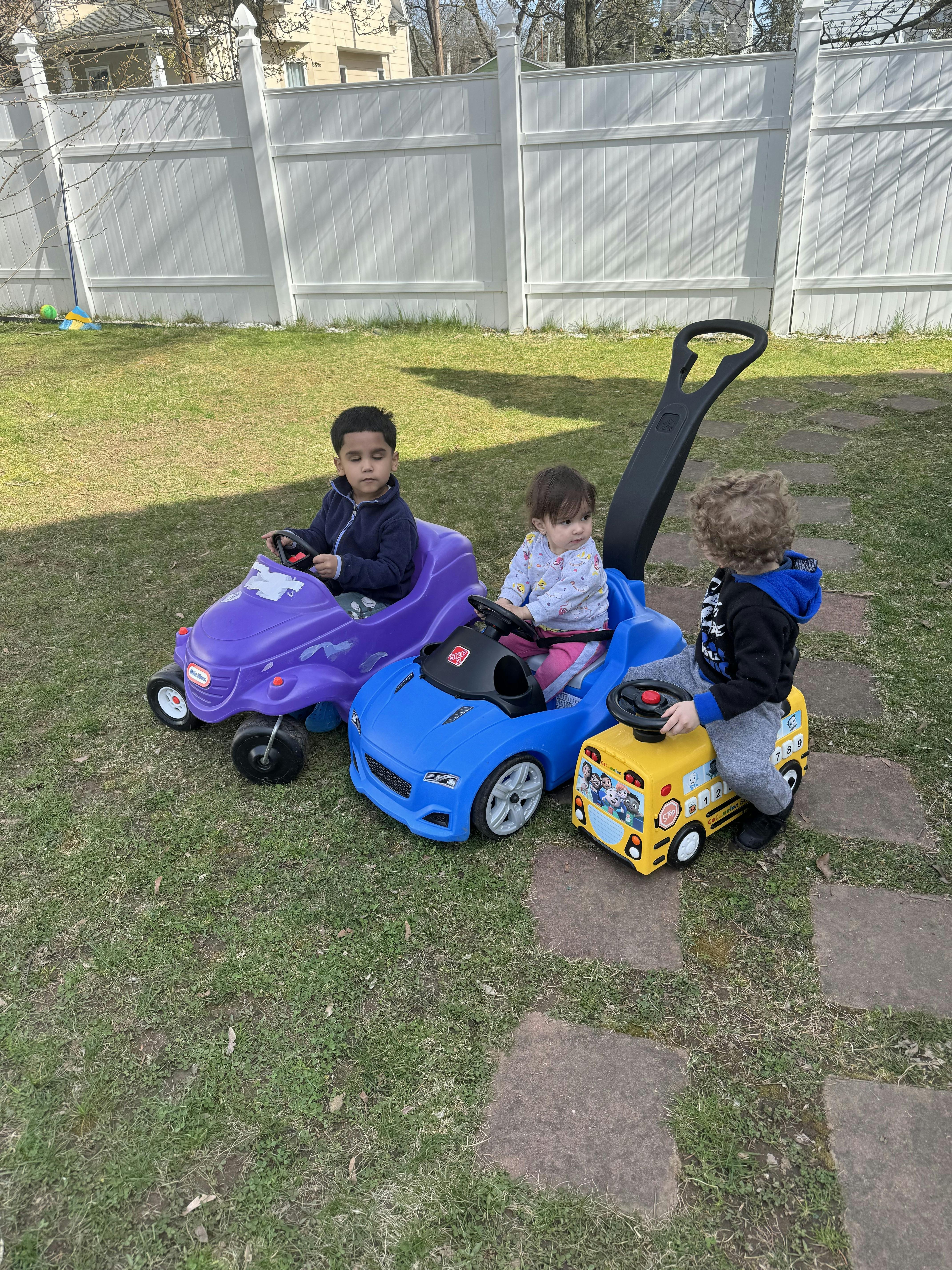Three children playing with ride-on toys in a grassy area