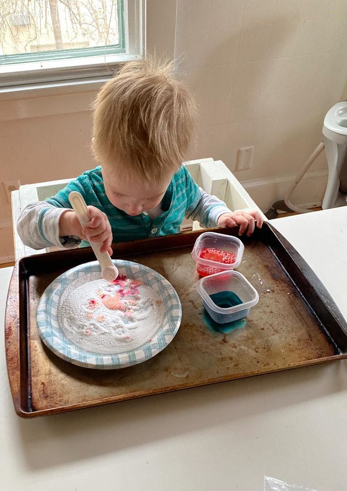 Child in a high chair mixing powder on a plate with a spoon