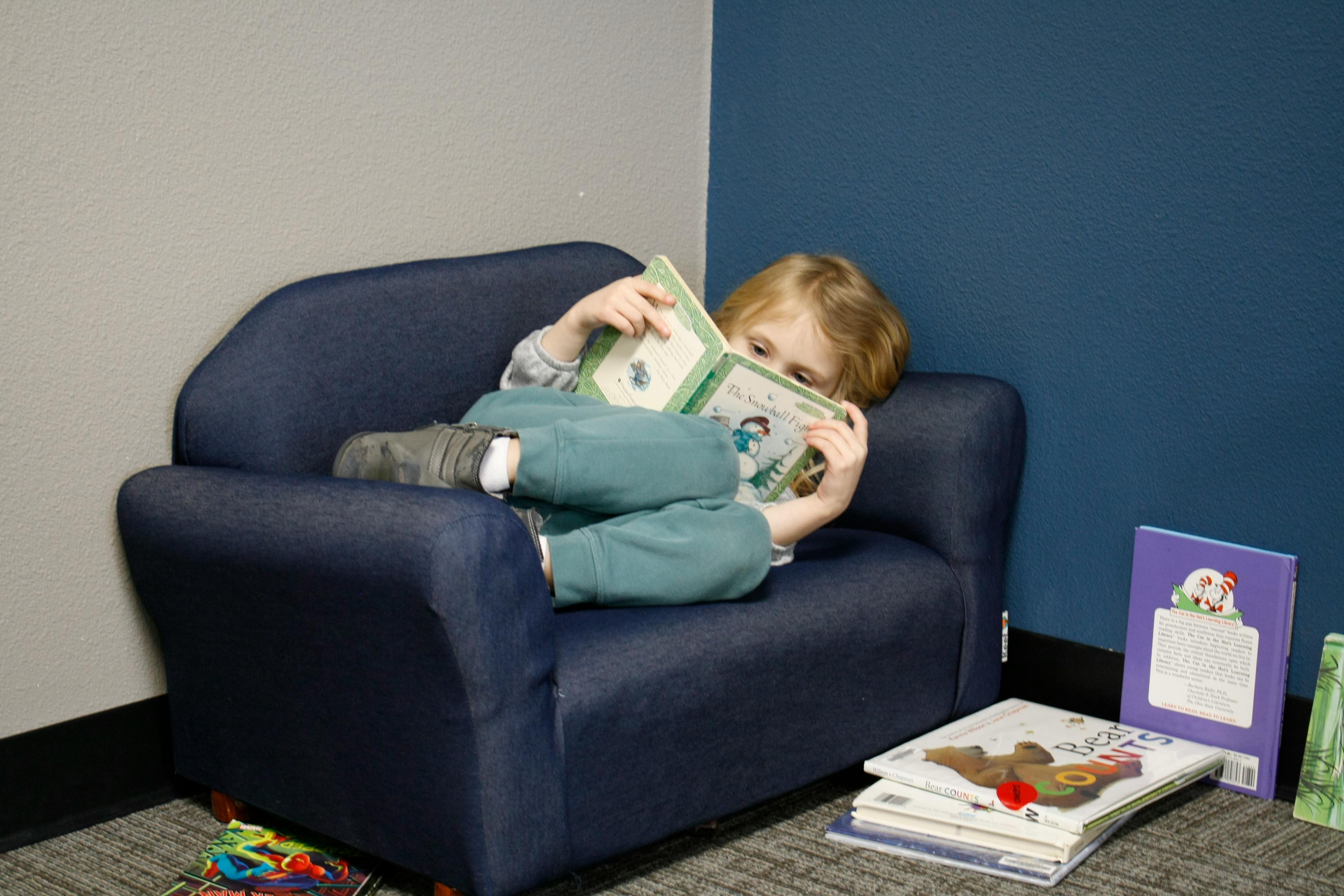 Child lying on a small couch reading a book