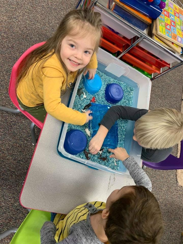 Three children playing with a sensory bin filled with blue material and green material