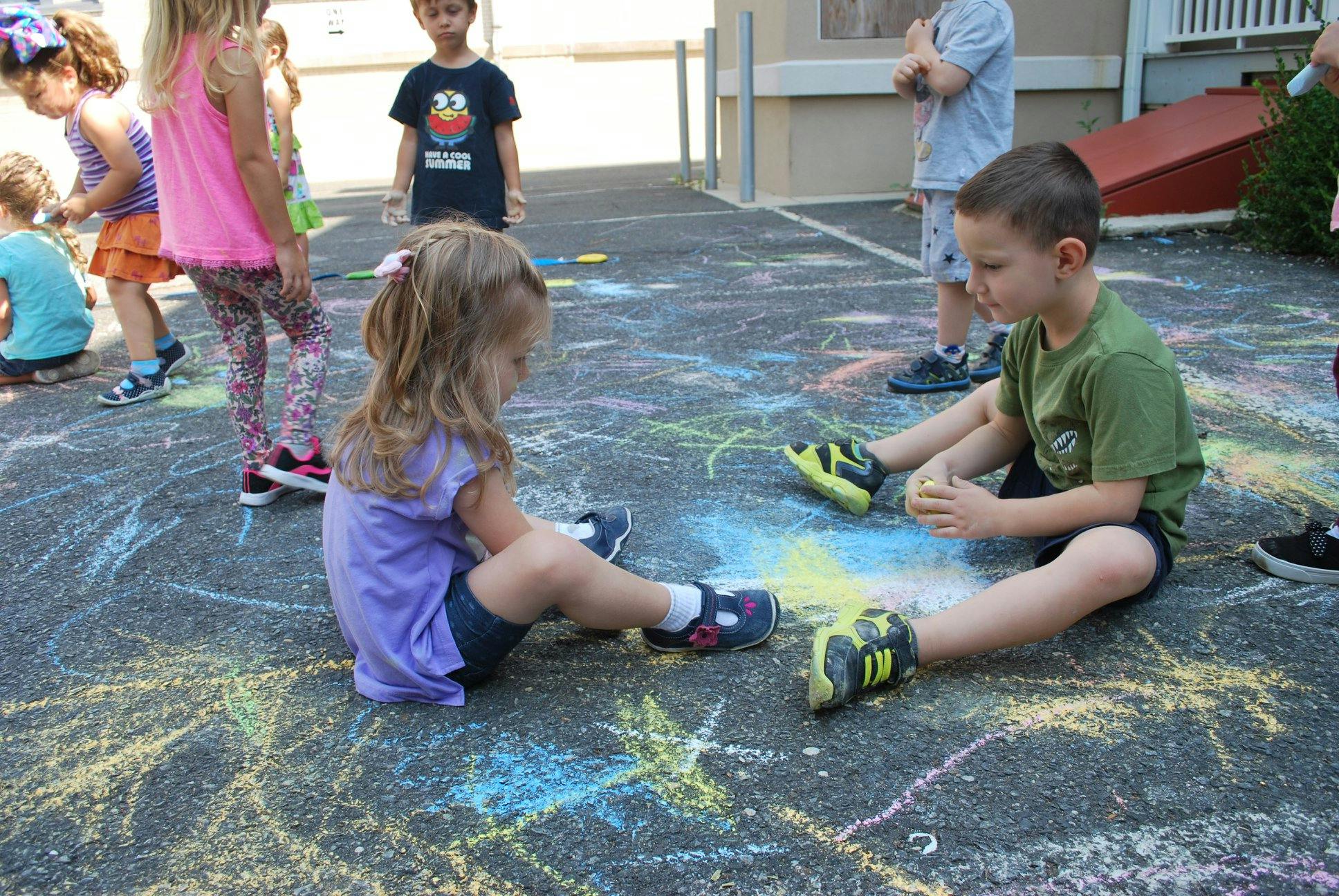 Two children sitting on pavement drawing with chalk