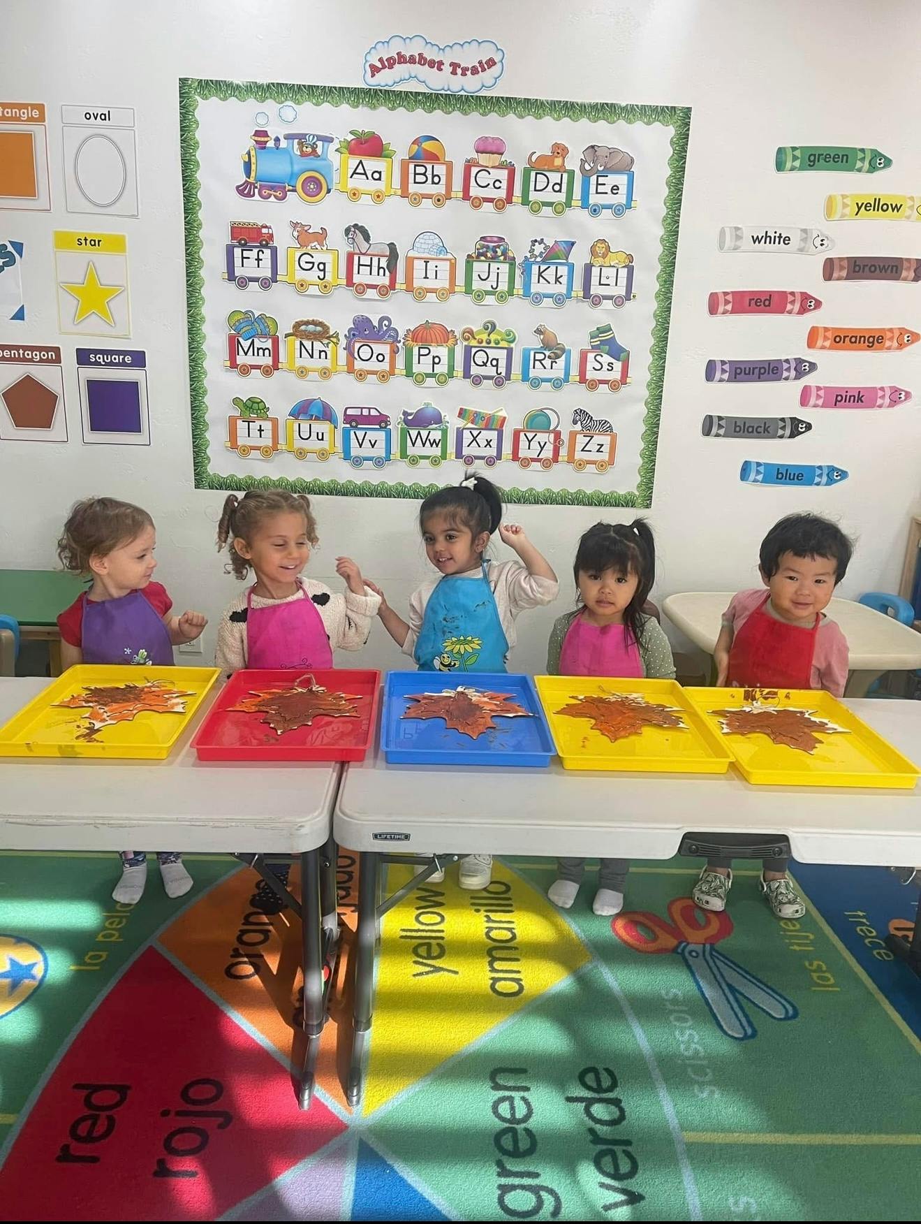 Five children at a table with art projects in trays
